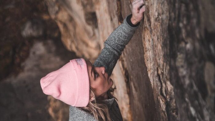 focused young sportswoman climbing huge cliff in ravine