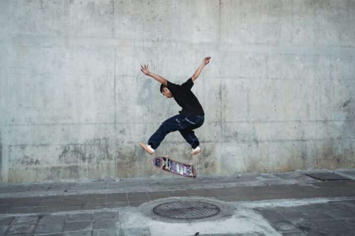 young man jumping with skateboard above manhole near concrete wall