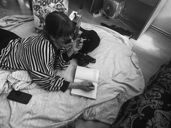 stylish woman smoking while writing in notebook on bed