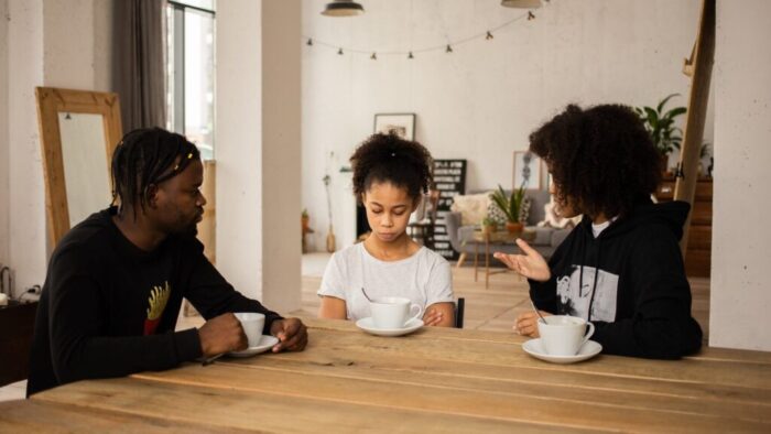 black parents lecturing upset daughter at table