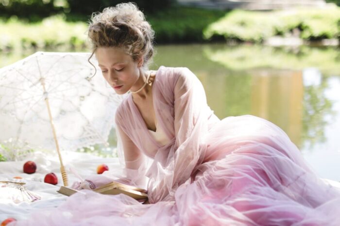 elegant woman in pink dress sitting on a picnic blanket while reading a book